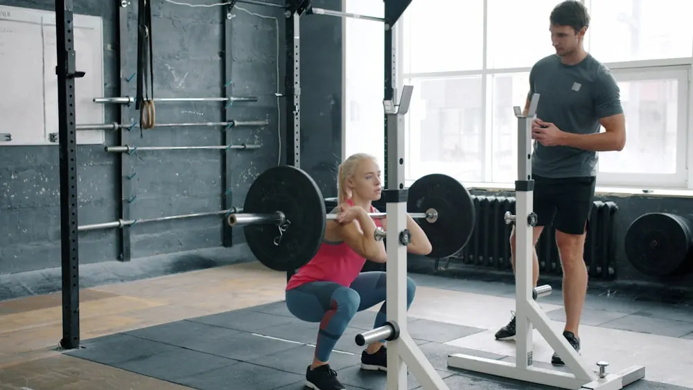 Member squatting a barbell while a coach watches her form